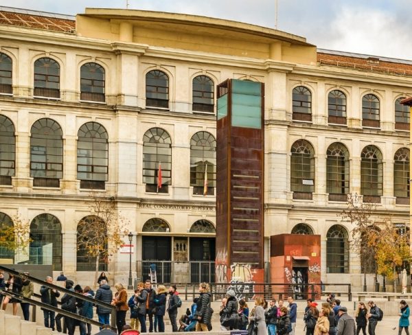 The Reina Sofia Museum in Madrid, displaying its neoclassical façade with a modern glass elevator, bustling with visitors at the entrance, capturing a moment of cultural engagement in the city.