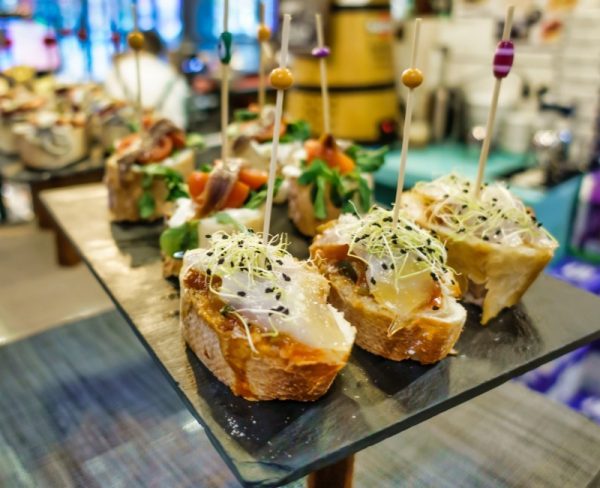 An array of Spanish tapas displayed on a glass surface, featuring crusty bread topped with various cheeses, meats, and garnishes, skewered with colorful toothpicks, ready to be enjoyed in a vibrant setting.