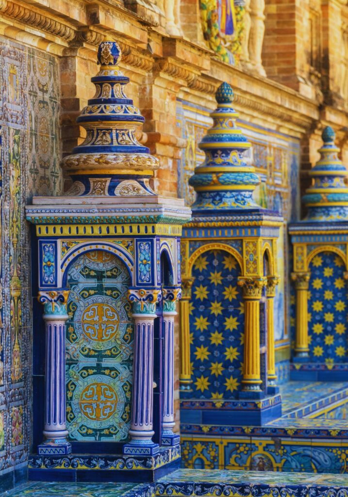 Close-up of colorful ceramic tilework and ornate columns in Plaza de España, Seville. The vibrant blues, yellows, and greens showcase traditional Andalusian craftsmanship and historical motifs.