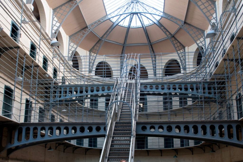 Interior of Kilmainham Gaol in Dublin, showcasing a large circular cell block with steel staircases, arched doorways, and a domed skylight that casts light over the prison’s tiers.
