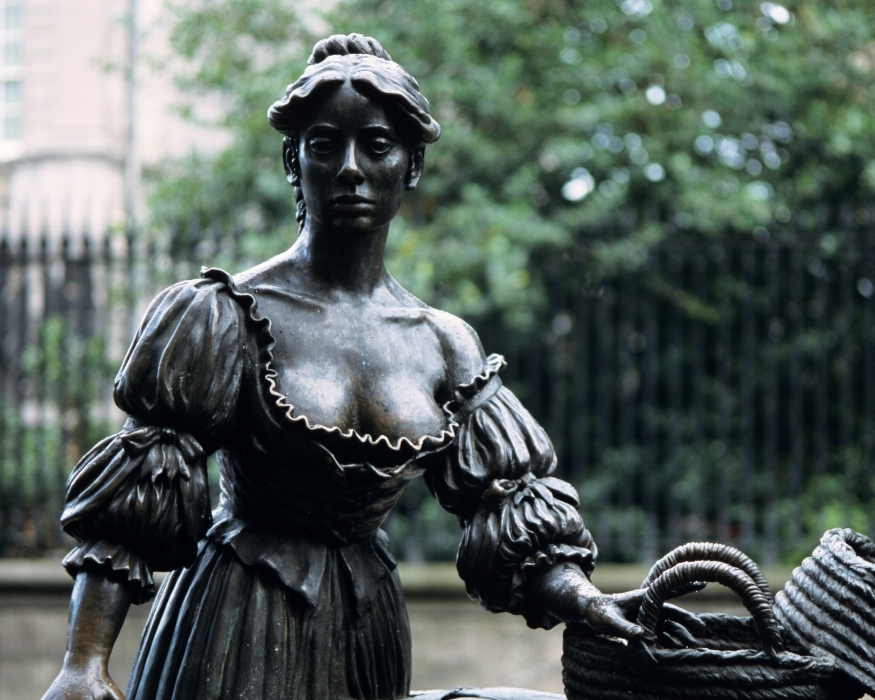 Close-up of the Molly Malone statue in Dublin, depicting a bronze woman in 17th-century dress with puffed sleeves, a low neckline, and one hand resting on a wicker basket, commemorating the famous Irish ballad character.