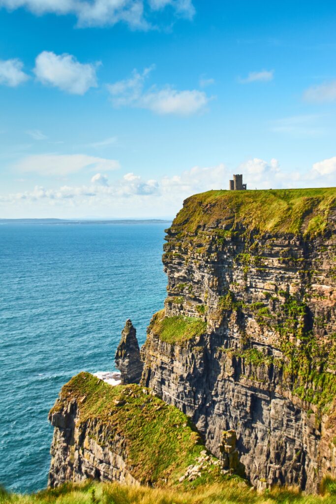 O'Brien's Tower sits atop a grassy cliff at the Cliffs of Moher, with clear blue skies and the Atlantic Ocean stretching out behind it, creating a picturesque and iconic Irish landscape.