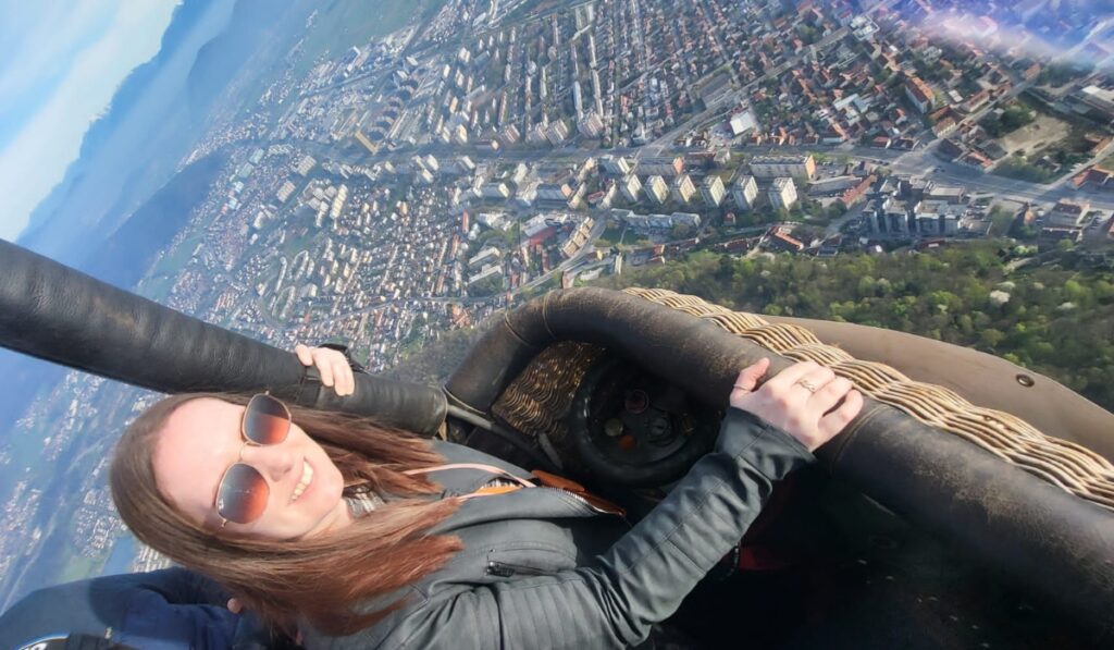 Me enjoying a hot air balloon ride high above Ljubljana, with a sweeping aerial view of the cityscape and distant mountains.