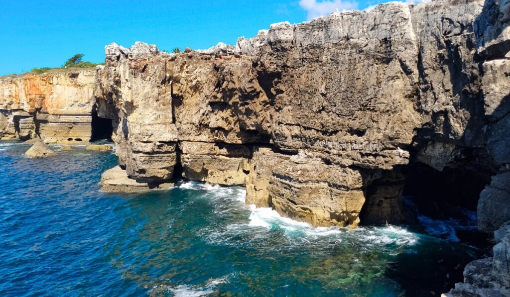 Close-up of the jagged cliffs and sea caves at Boca do Inferno, with turquoise water swirling at the base of the textured stone wall.