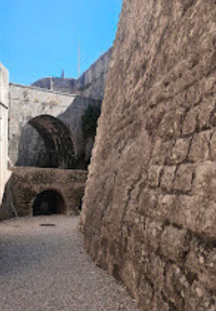 Stone passageway inside the Cascais Citadel, showing weathered fortress walls and arched tunnels under a clear blue sky. The historic architecture highlights the citadel’s military past and coastal defense design.