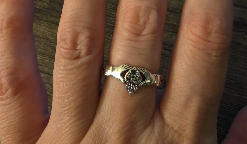 Close-up of a silver Claddagh ring worn on a hand, featuring two hands holding a heart topped with a crown, symbolizing love, loyalty, and friendship.