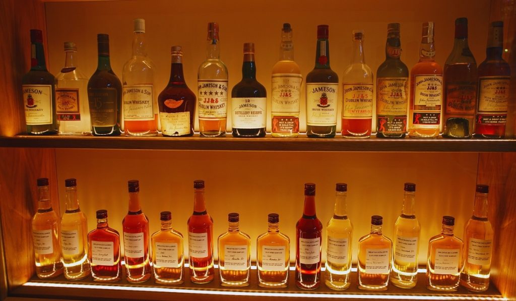 A warmly lit whiskey display featuring a variety of Jameson and Midleton Irish whiskey bottles, showcasing labels from different eras and blends.