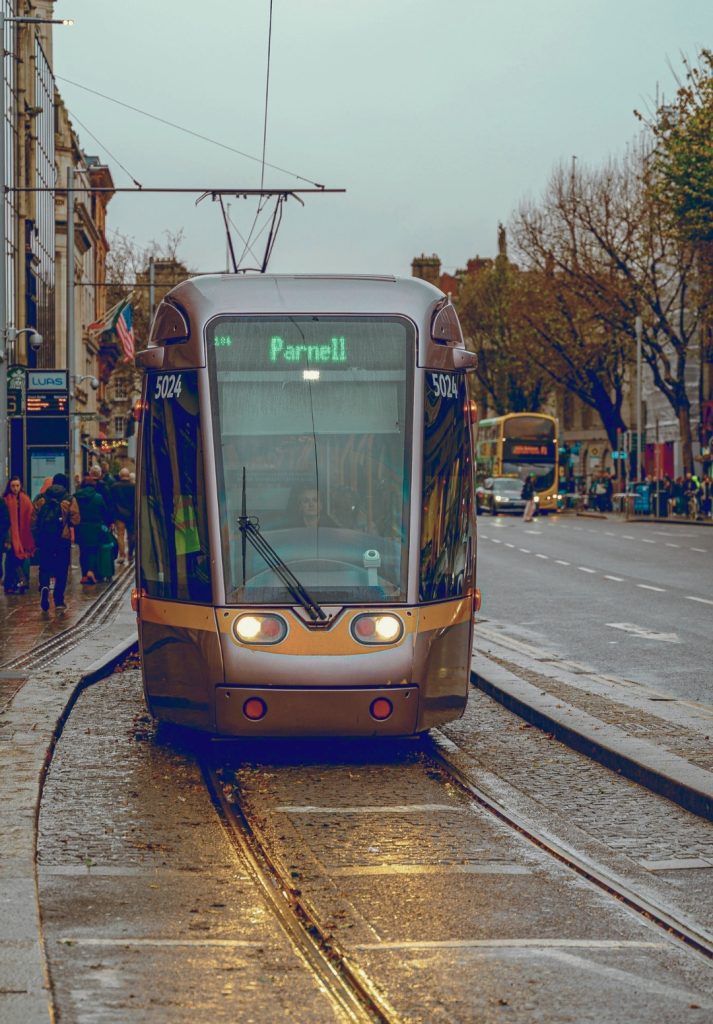 A Luas tram bound for Parnell glides along wet tracks on a rainy day in Dublin, Ireland, surrounded by pedestrians and city traffic. The image captures everyday transit during winter in Dublin.