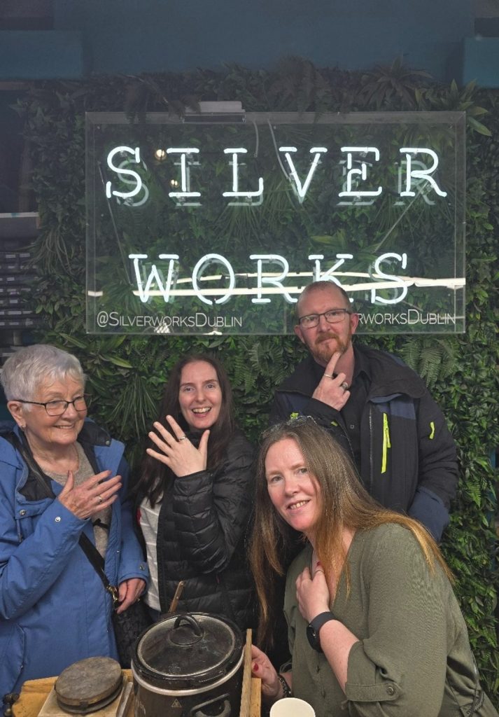 My family in front of a neon “Silver Works” sign, proudly displaying silver rings on their fingers, with greenery and jewelry tools visible in the background.