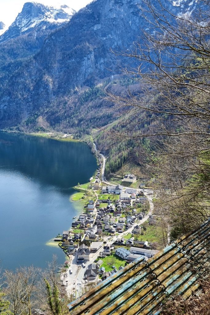 A high-angle view of Hallstatt’s lakeside village, with clustered alpine houses and winding roads beside the deep blue lake and backed by steep mountain cliffs.