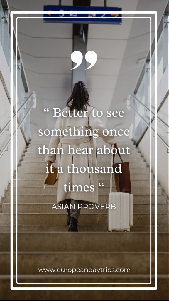 Traveler seen from behind climbs a wide station staircase in a cream coat, pulling a white suitcase and carrying a brown tote and tan hat, framed by glass railings and overhead platform signs. Overlaid text reads "Better to see something once than hear about it a thousand times" and "ASIAN PROVERB" with "europeandaytrips.com
" at the bottom.