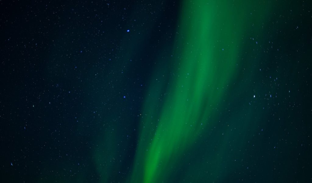 Green northern lights stretch across a dark, starry sky.