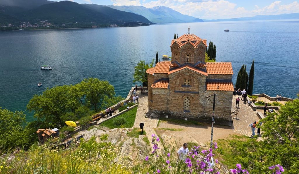 Saint John at Kaneo sits on a cliff above Lake Ohrid with red tiled roofs and blue water stretching toward distant mountains.