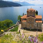 Saint John at Kaneo sits on a cliff above Lake Ohrid with red tiled roofs and blue water stretching toward distant mountains.