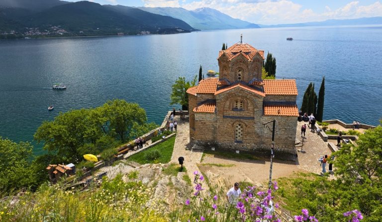 Saint John at Kaneo sits on a cliff above Lake Ohrid with red tiled roofs and blue water stretching toward distant mountains.