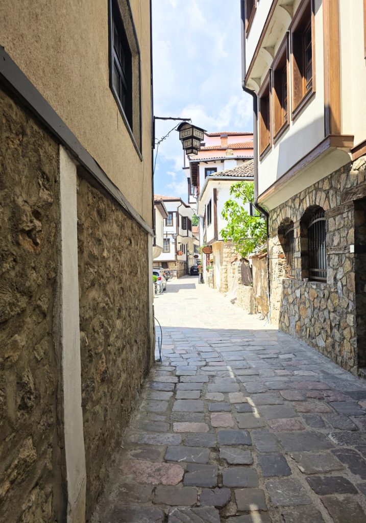 A narrow cobblestone street runs between stone and whitewashed buildings in Ohrid Old Town.