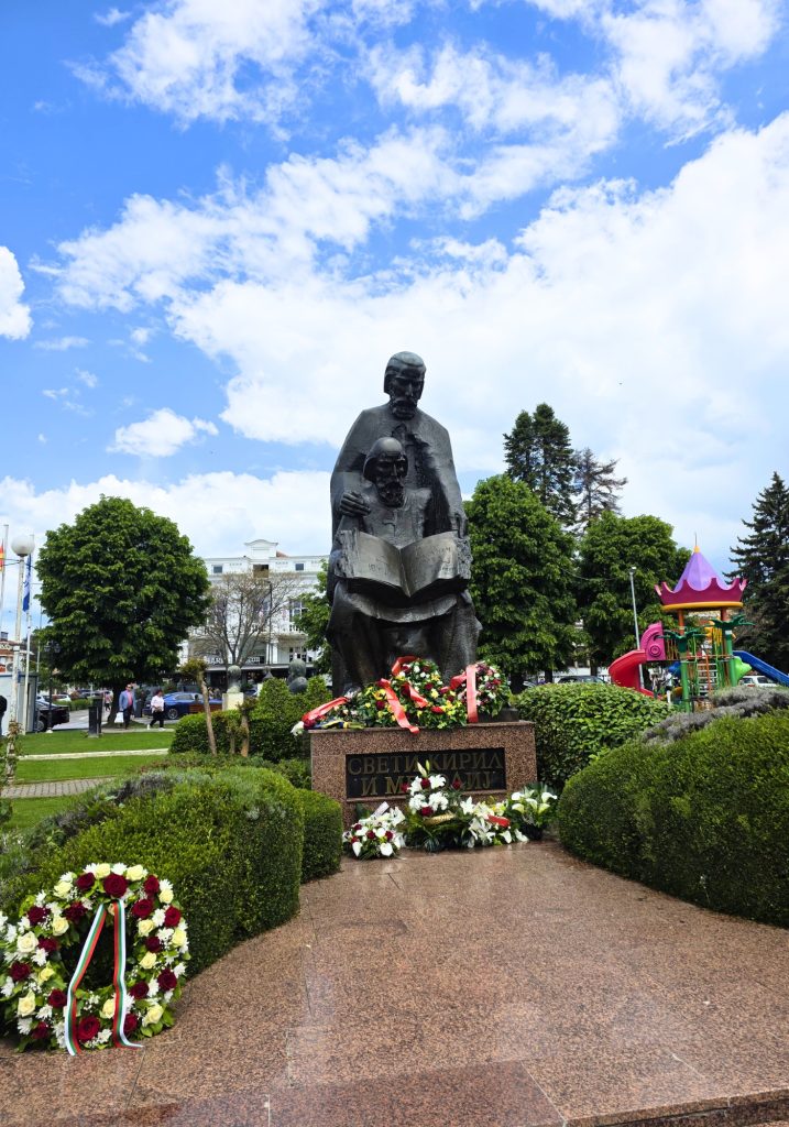 A statue of Saints Cyril and Methodius stands in a landscaped square with floral wreaths and the text "СВЕТИ КИРИЛ И МЕТОДИЈ" on the base.