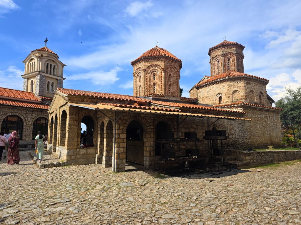 Saint Naum monastery in Ohrid has arched walkways red tiled domes and visitors walking across the cobblestone courtyard.