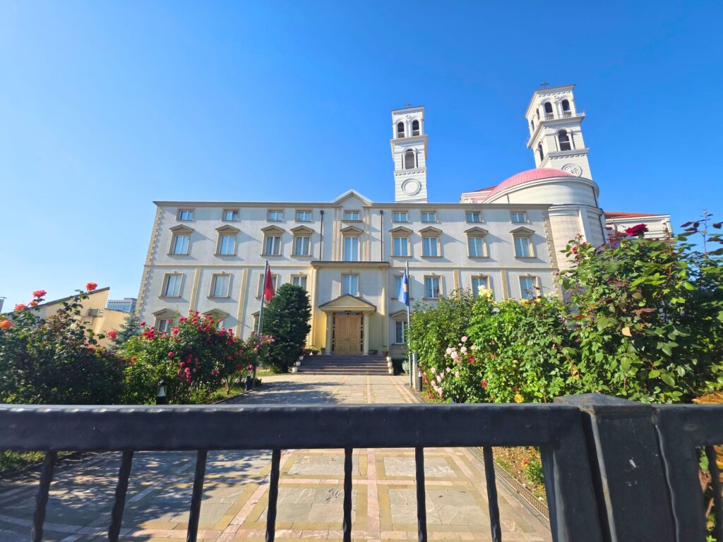 Front of Mother Teresa Cathedral in Pristina, with twin bell towers and a garden-lined path to the entrance.