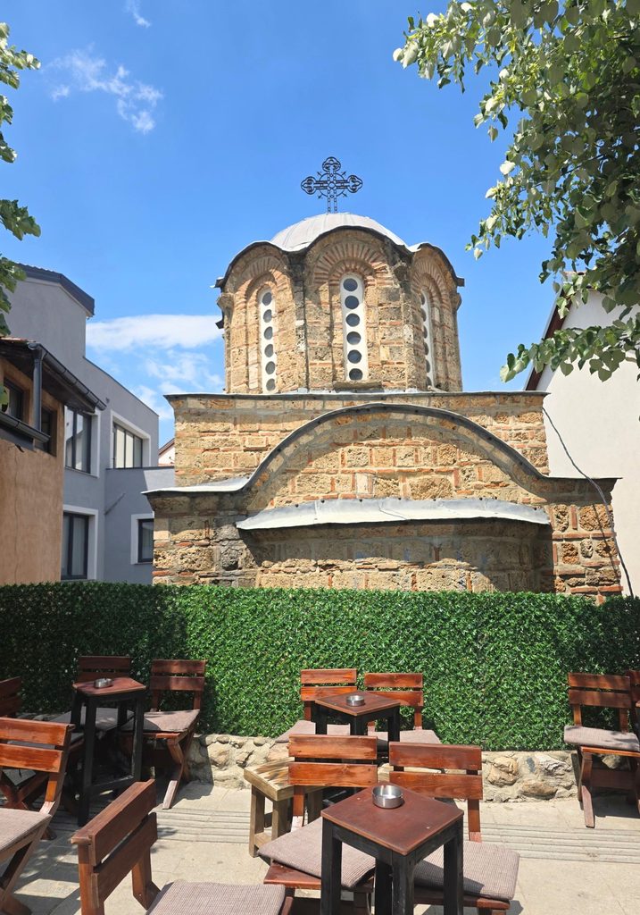 Church of St Nicholas in Prizren, with patterned stonework and a domed tower behind an outdoor seating area
