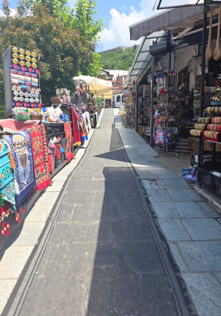 Narrow shopping street in Prizren lined with stalls selling colourful textiles, clothing and souvenirs.